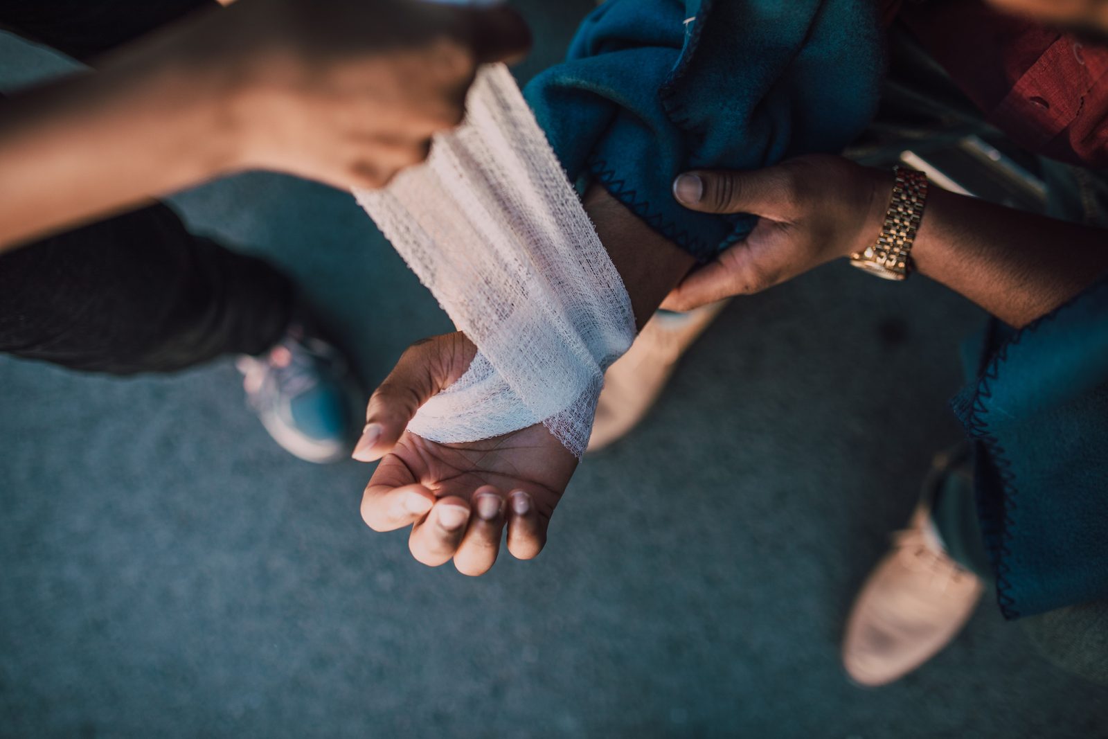 Gloved hands wrapping a bandage around a person's hand outdoors