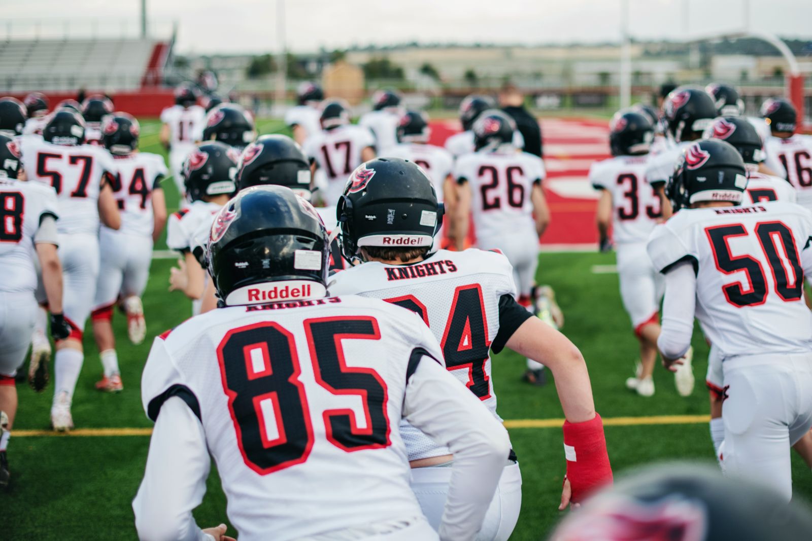A high school football team in uniform running onto the field before a game
