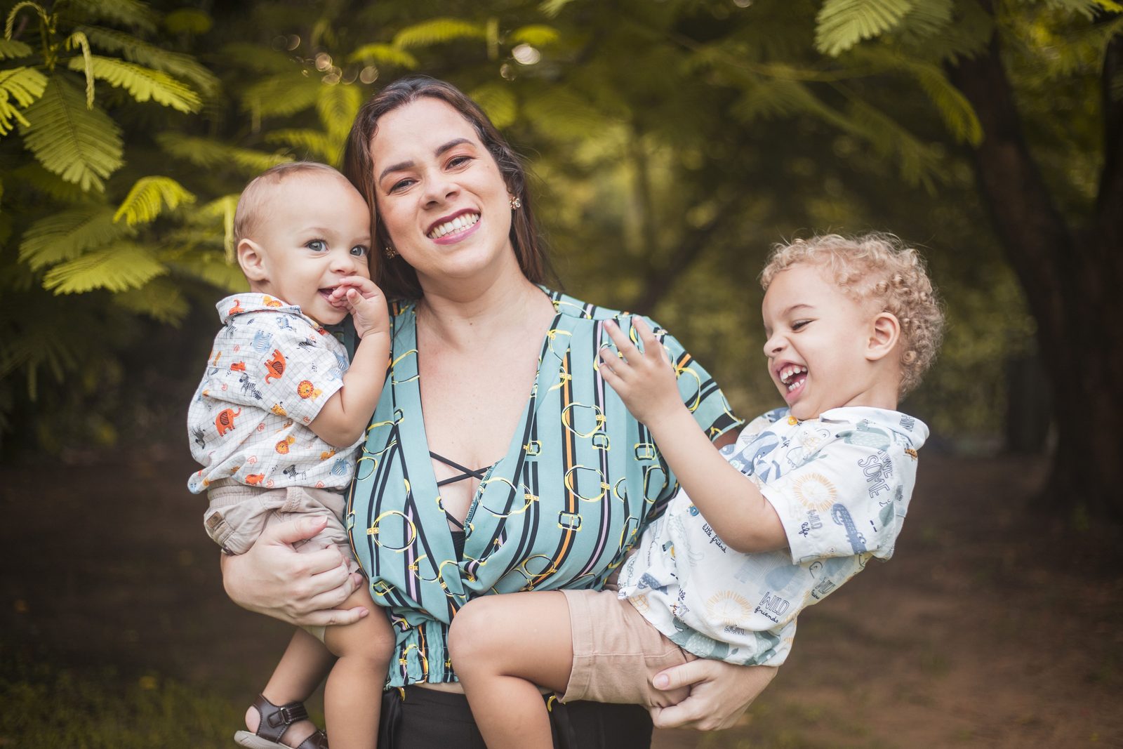 A mother outdoors holding her baby with her older child beside her
