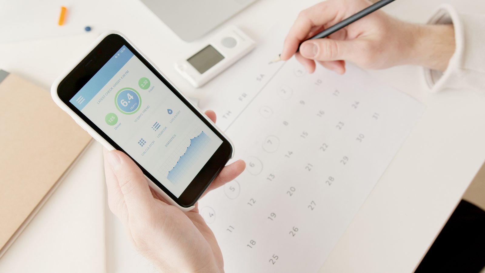 Hands holding a phone showing a schedule app above a paper calendar