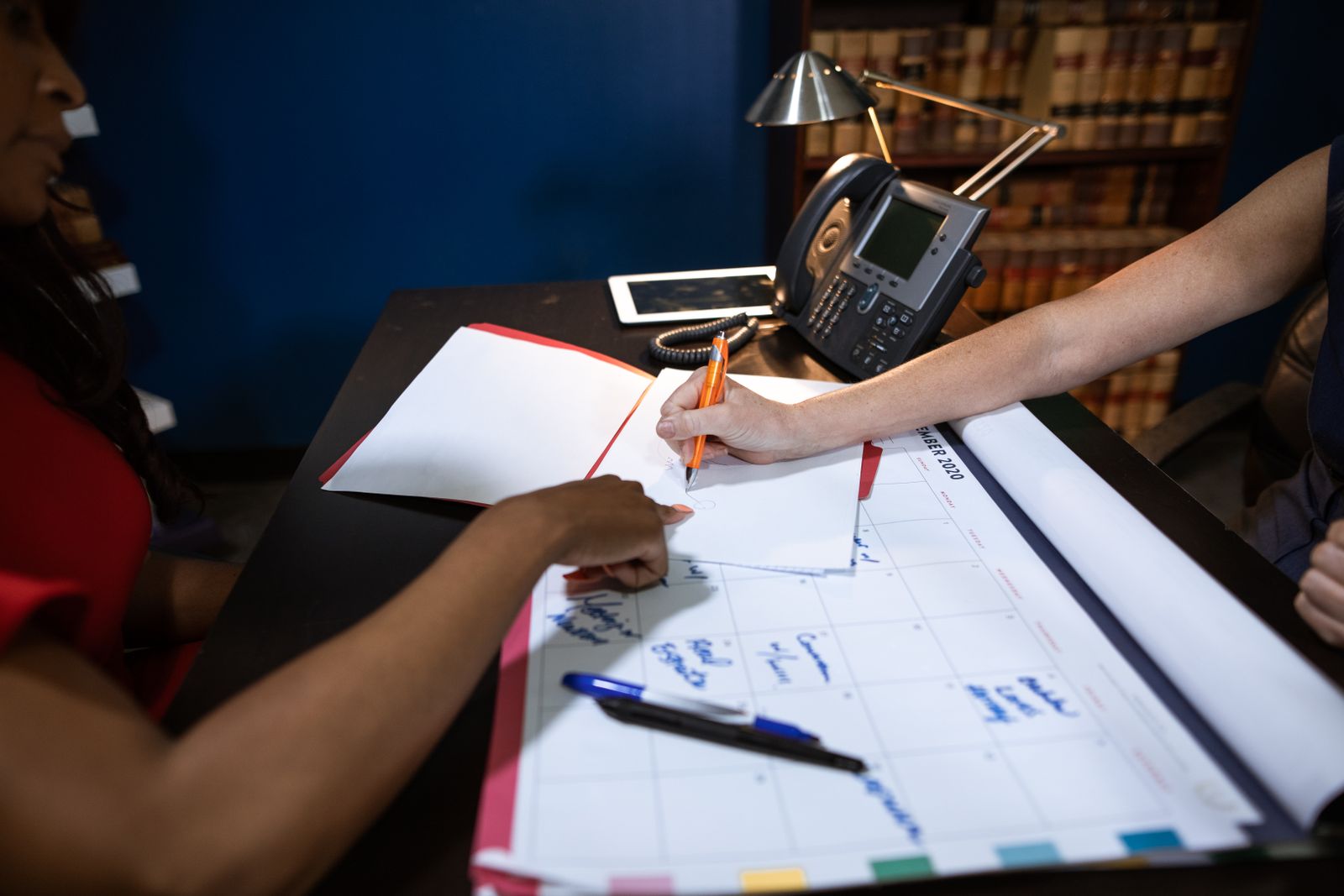 Two people marking dates on a large wall calendar spread across a desk