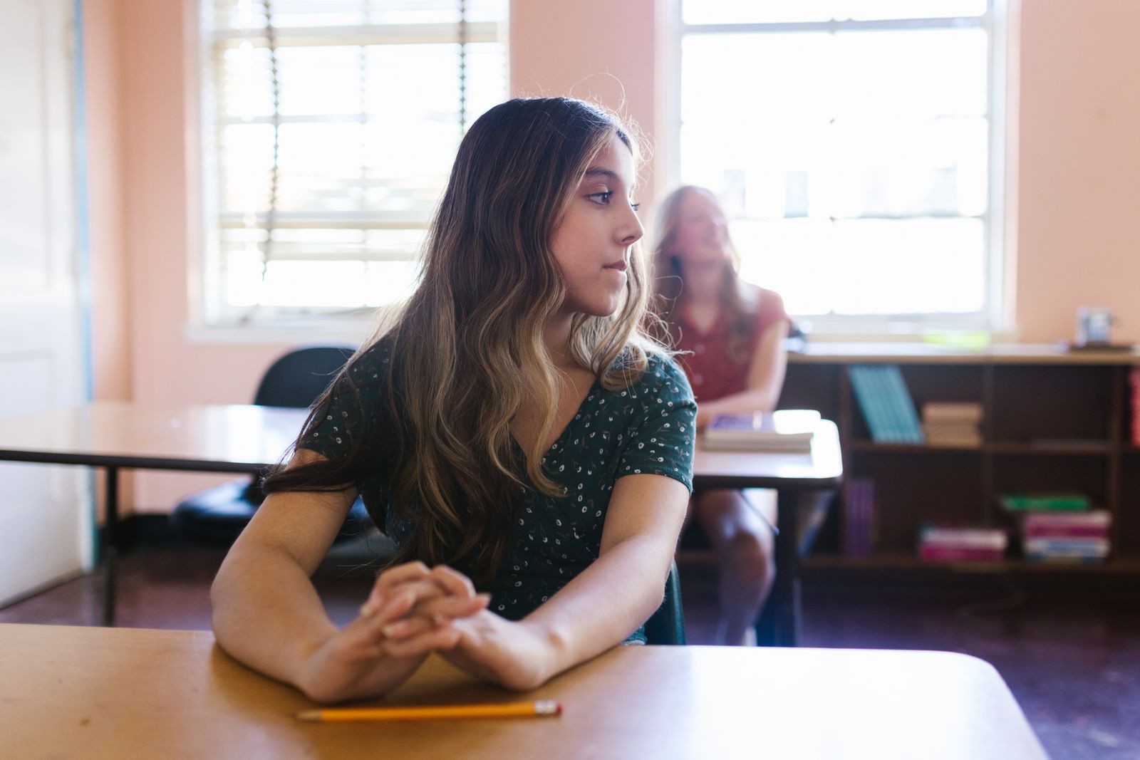 A student sitting quietly at a classroom desk beside a sunlit window
