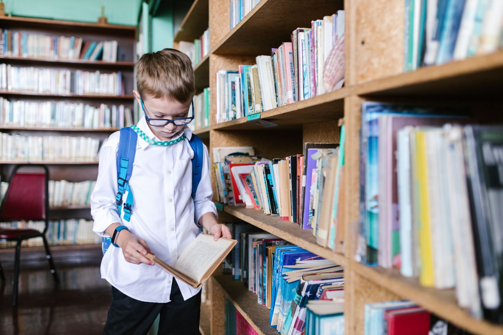 A student wearing glasses reading a book in a school library
