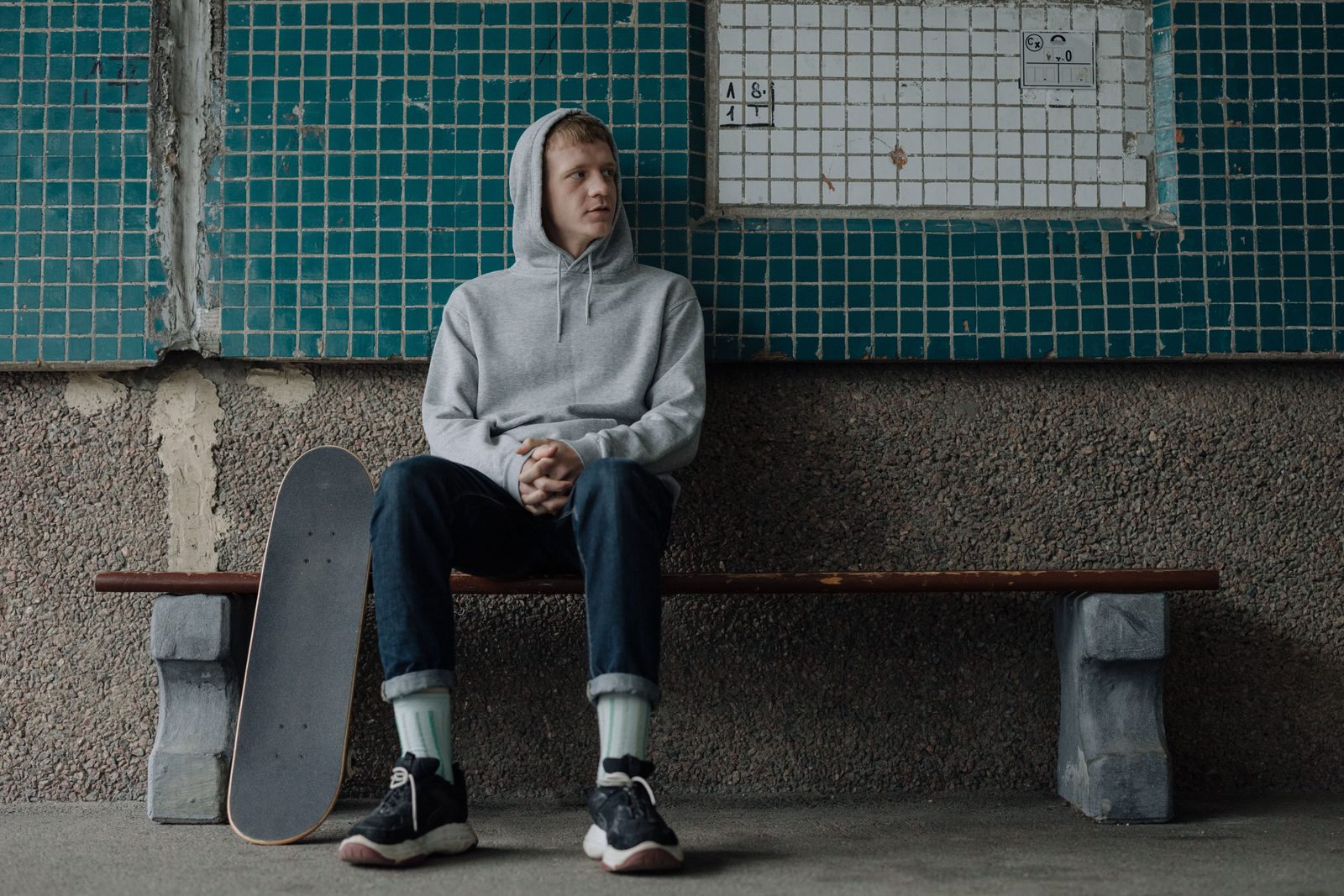 A teenager sitting alone on a bench with a skateboard