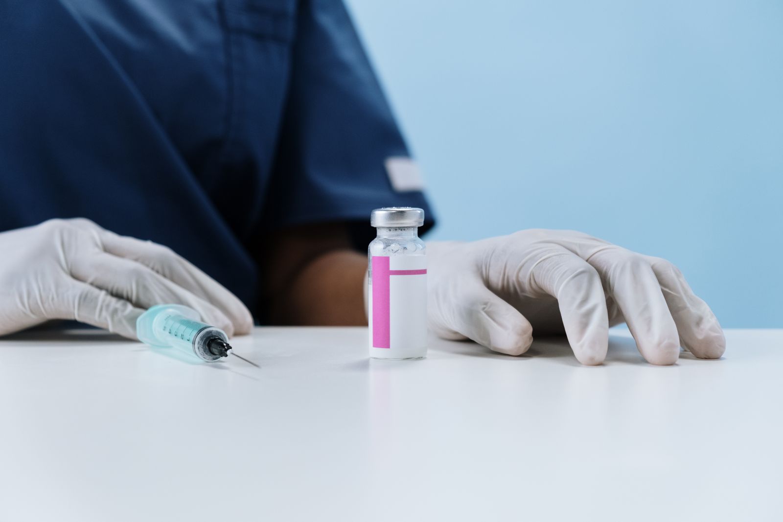 A clinician in gloves with a vaccine vial and syringe prepared on a table