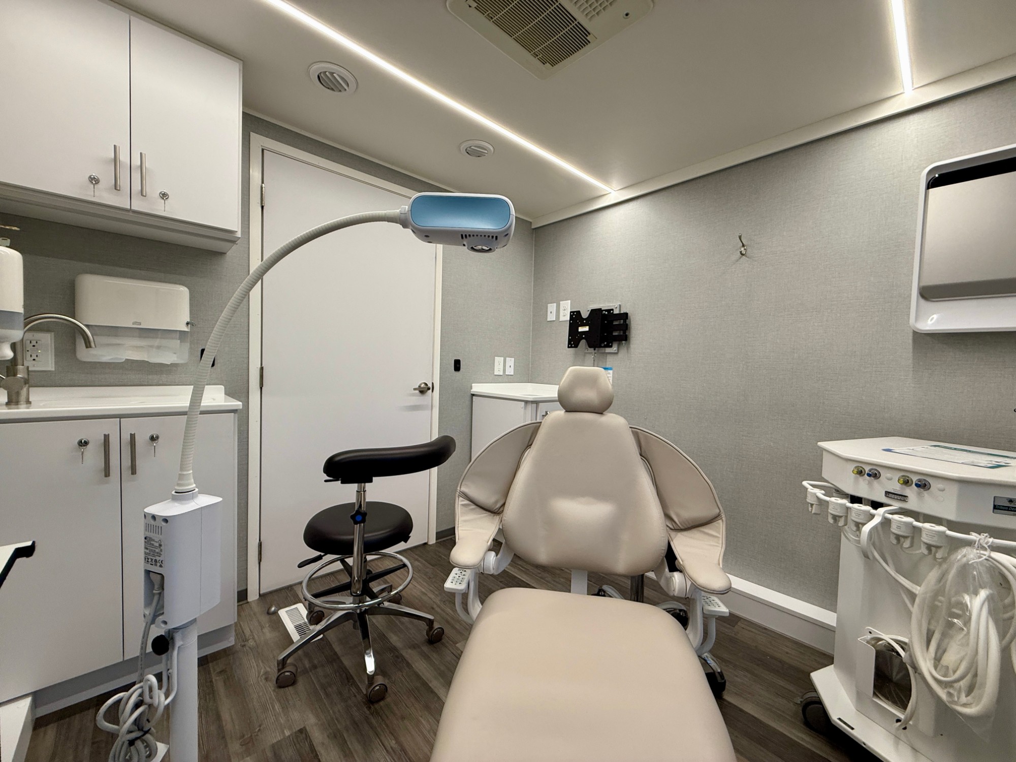 Chairside view of a dental operatory with delivery unit, exam light, and clinician stool