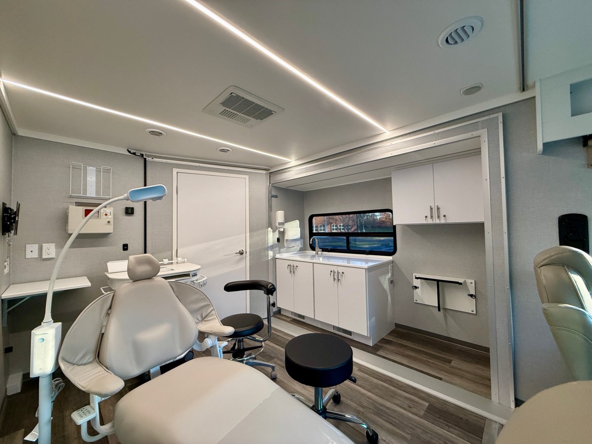 Mobile dental operatory with treatment chair and exam light beside an expanded slide-out room with sink and storage