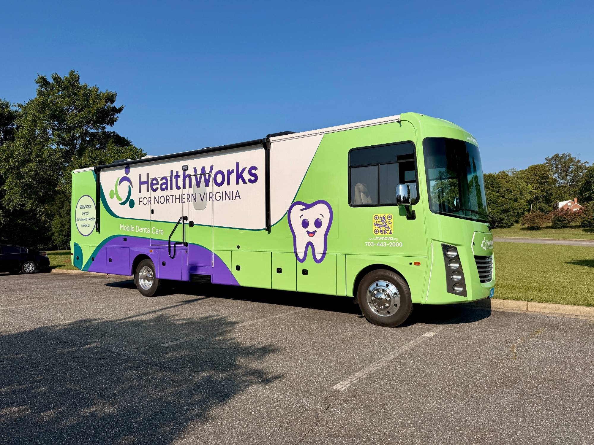 A HealthWorks for Northern Virginia mobile dental clinic parked outdoors, wrapped in green and purple with a smiling tooth graphic