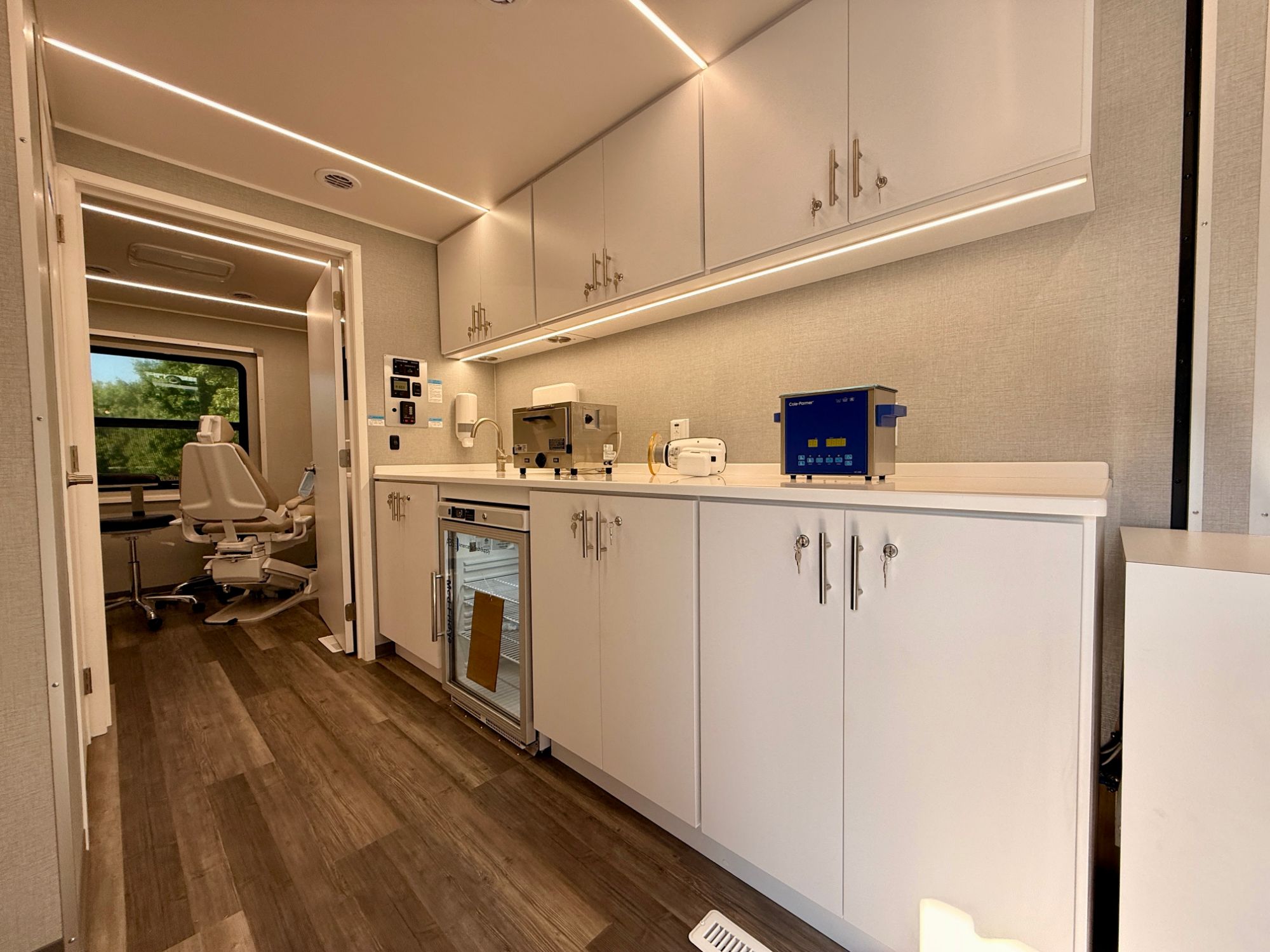 Sterilization and lab run with autoclave, ultrasonic cleaner, and refrigeration, with the operatory visible through the doorway