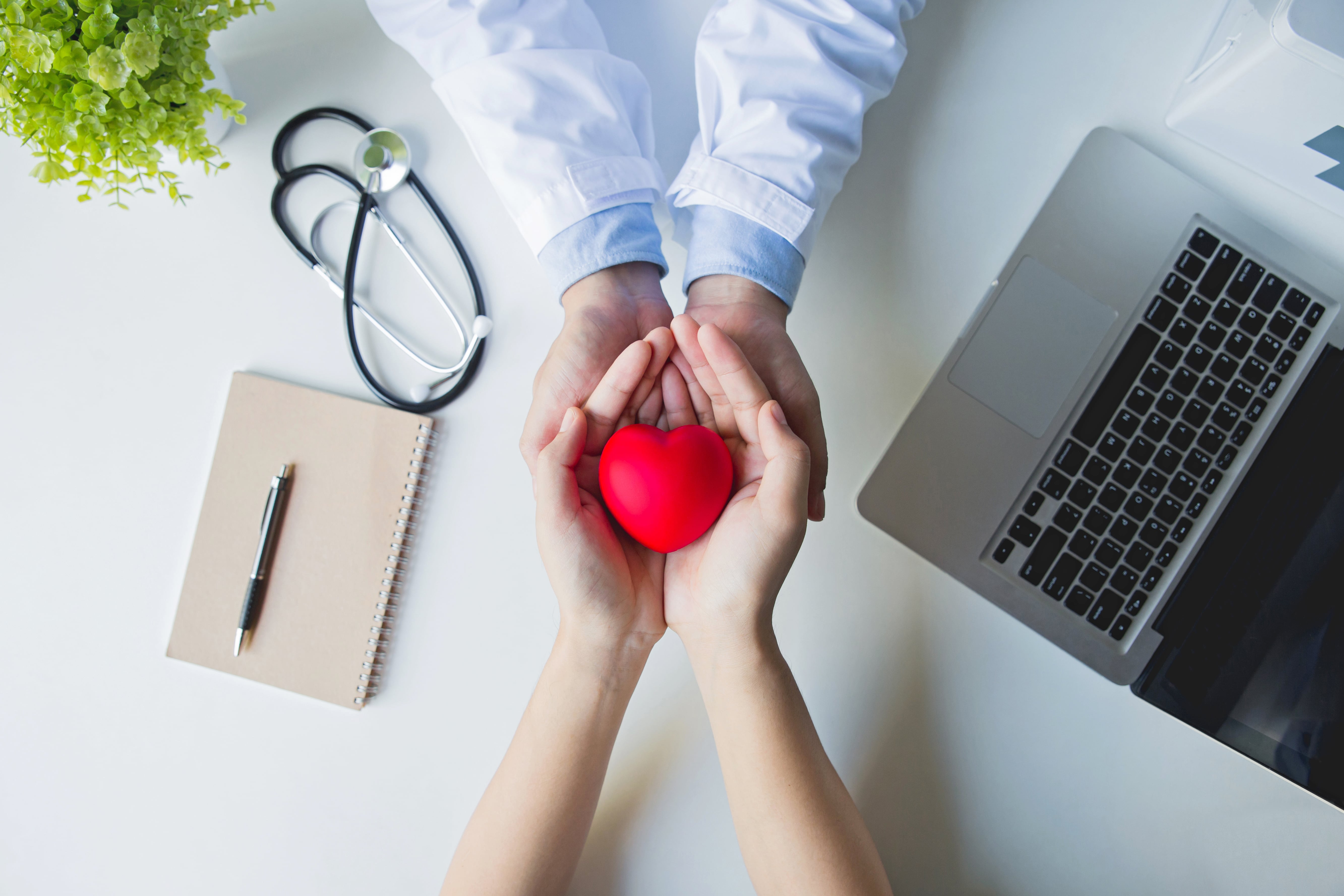 top-view-doctor-patient-hands-holding-red-heart-white-table-min