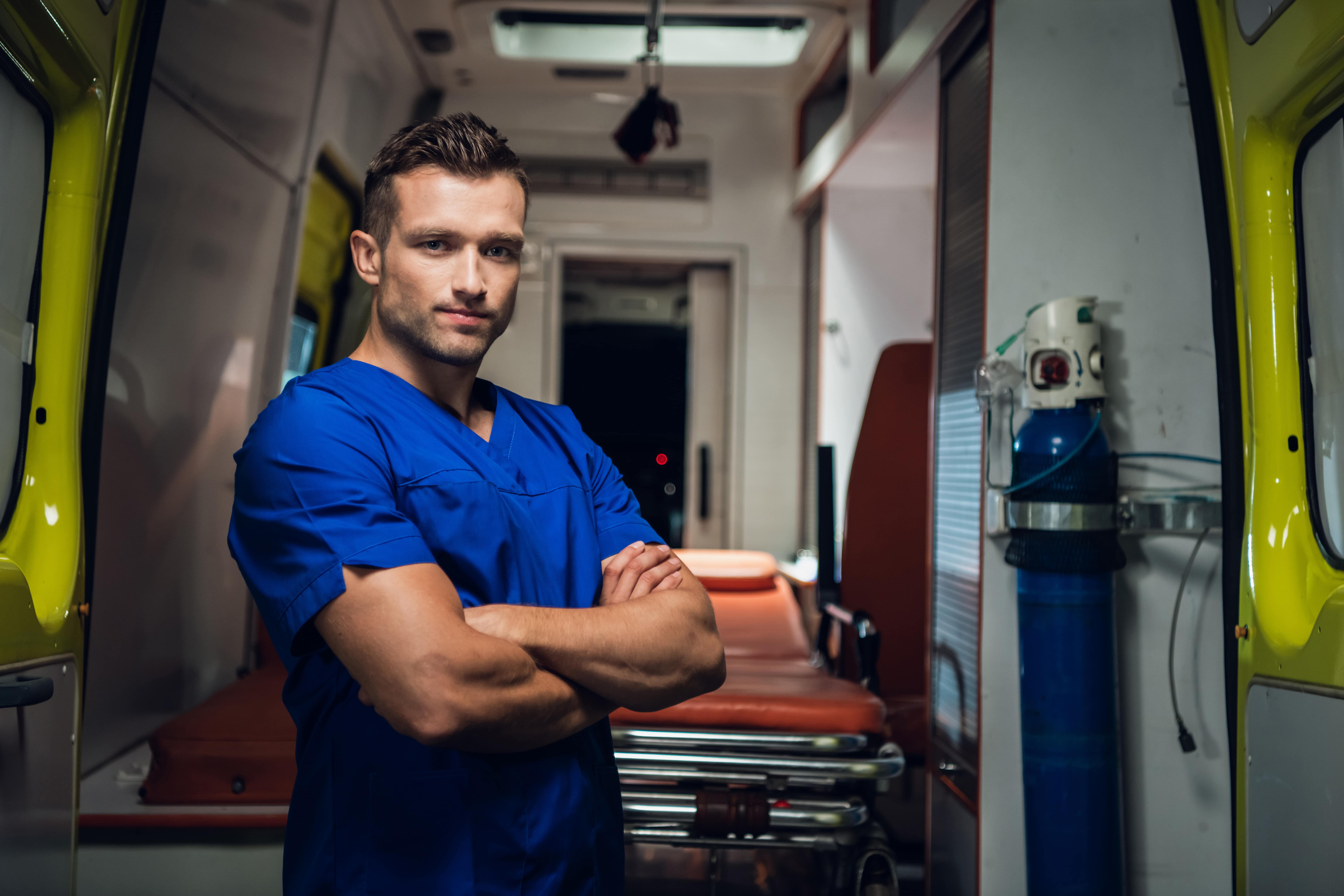 young-paramedic-looking-camera-smiling-ambulance-car-background-min