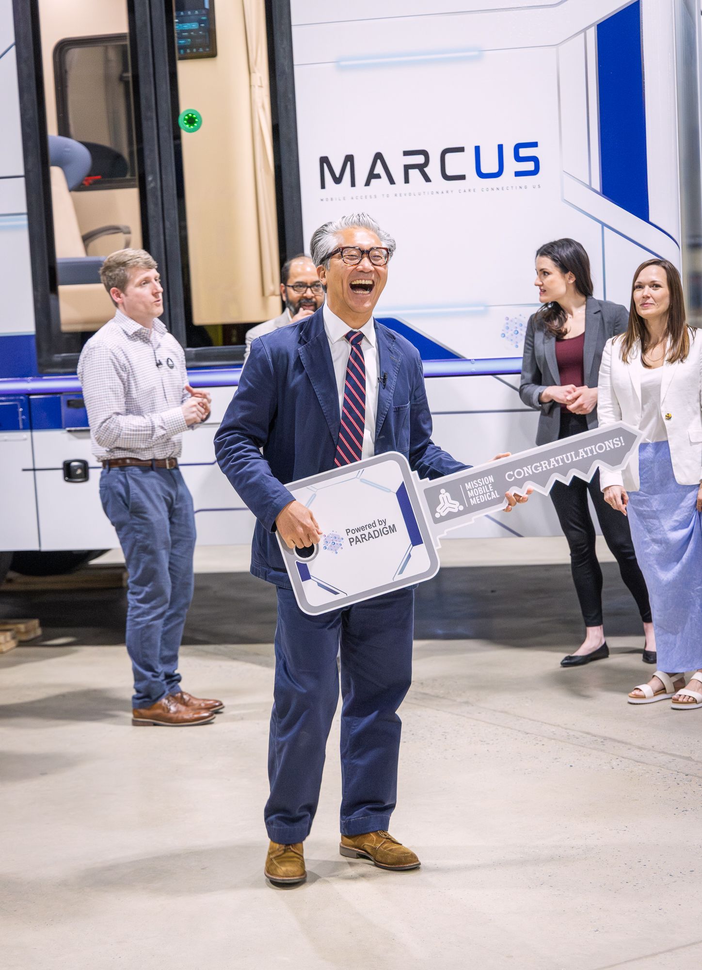 A visitor holding an oversized ceremonial key reading Congratulations, Powered by PARADIGM, laughing in front of MARCUS